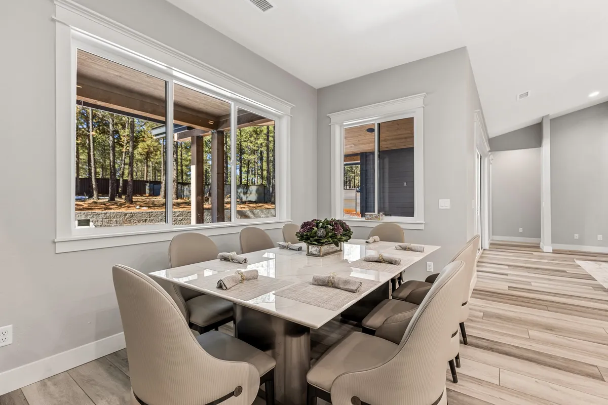 This image presents an elegant dining area with a sizable dining table set near large windows that offer abundant natural light and outdoor views. The ambiance is warm and welcoming, perfect for both casual breakfasts and festive dinner parties.