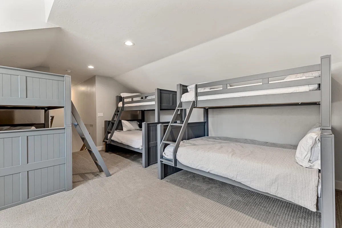 A playful bunk room with three sets of bunk beds, cozy carpet flooring, and an angled ceiling. The inviting setup promises fun sleepovers and group adventures.