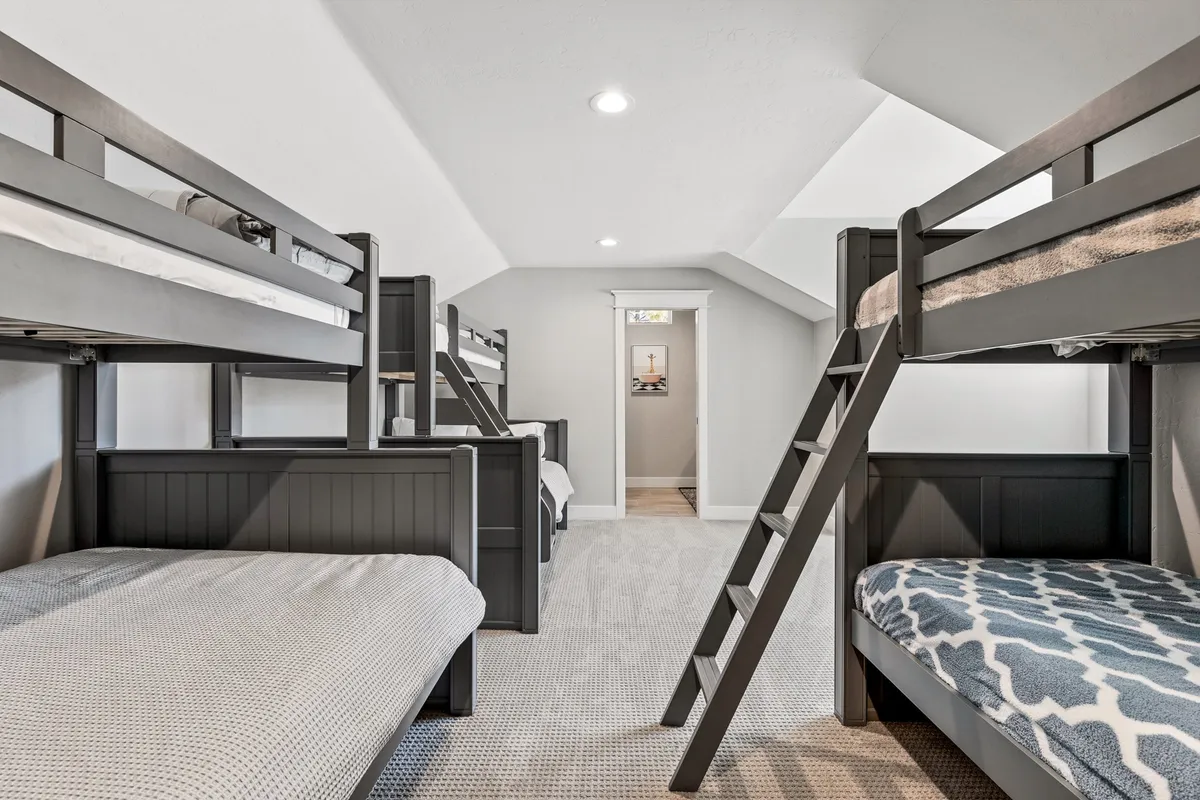 The image features a playful and relaxed kids' bunk room with bunk beds, a ladder, and a doorway leading to another room. The setting is designed for fun, sleepovers, and bedtime stories—emphasizing that the home is perfect for families with children.