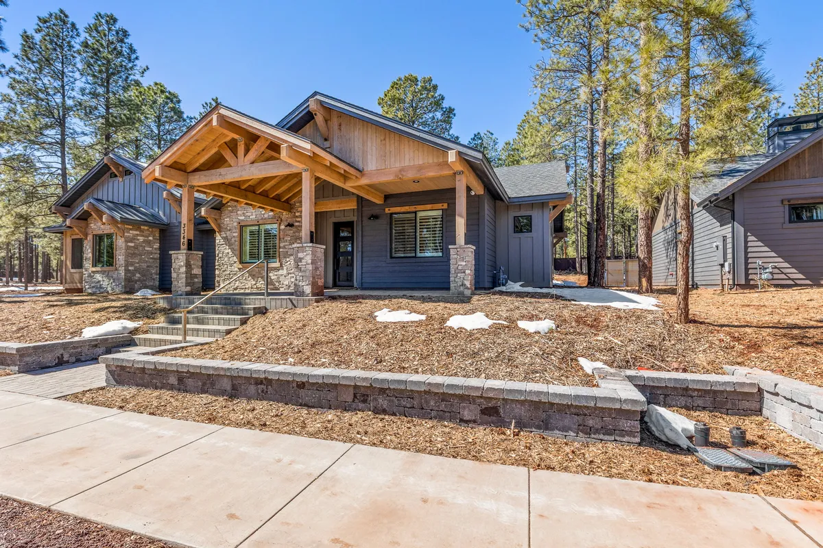 The front porch of the home is featured, framed by warm wooden beams and stone accents, and set against a beautifully landscaped yard. This inviting space connects the indoors to the outdoors and encourages relaxation while immersed in nature.