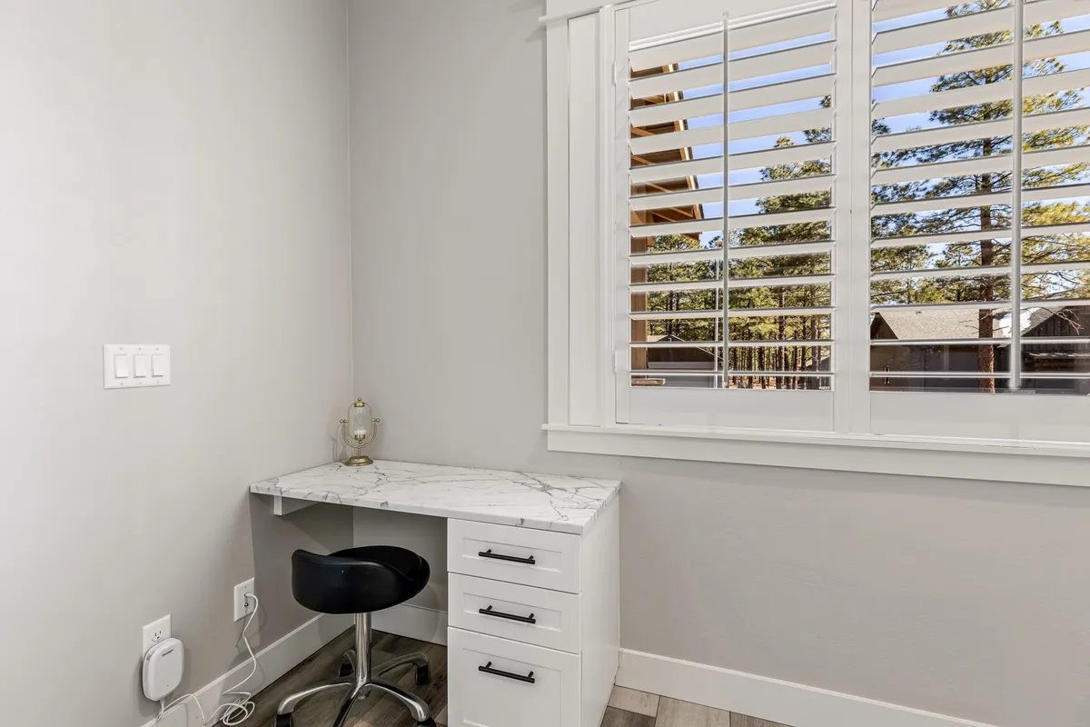 A focused workspace featuring a desk with a marble top, a stylish chair, and a window with blinds letting in natural light. The setting is calm and conducive to productivity, ideal for remote work or study.