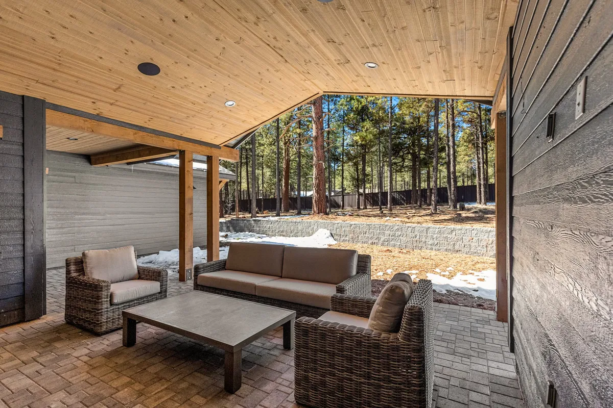 A tranquil backyard setting featuring a plush outdoor sofa, armchairs, and coffee table, surrounded by towering pine trees. The arrangement is inviting for morning coffee, social gatherings, or quiet reflection in nature.