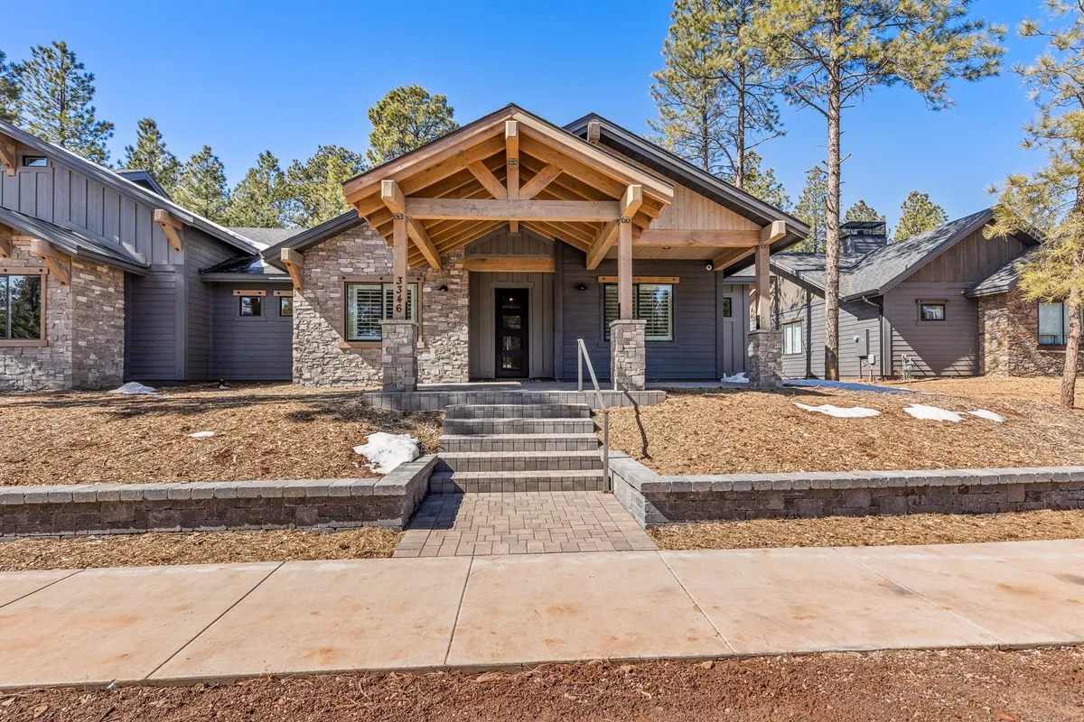 An inviting front porch with stone steps and wooden beams, surrounded by a landscaped yard and mature trees. The porch offers comfortable seating and is positioned to capture views of the sky and natural surroundings.
