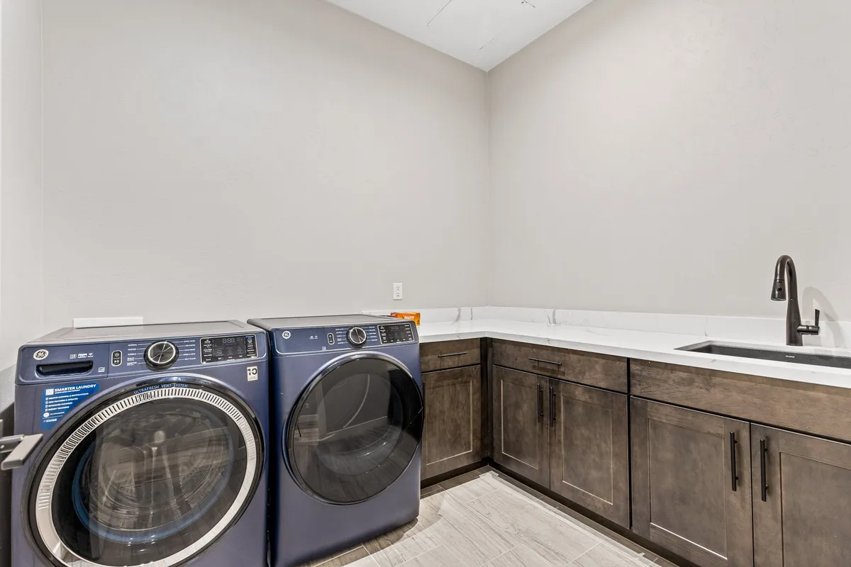 A dedicated laundry area with a modern washer, dryer, sink, and countertop for folding clothes. The space is organized and efficient, reflecting modern convenience and thoughtful design.