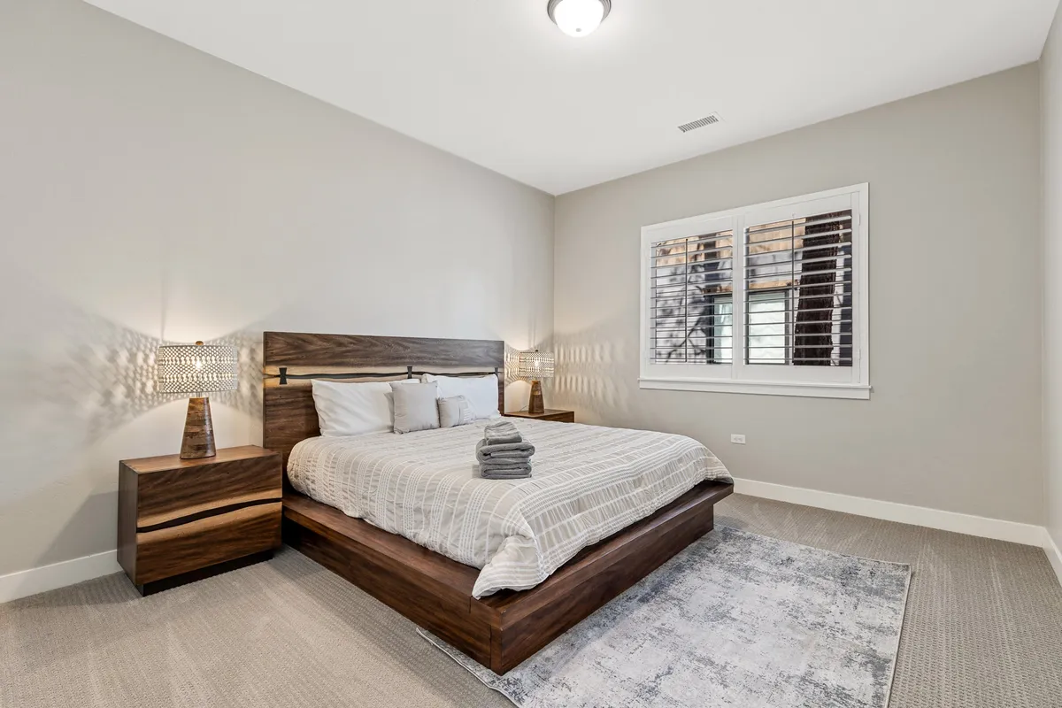 A serene bedroom with a comfortable bed, nightstands, soft lamps, and a large window framing views of the pines. Natural light fills the space, highlighting premium linens and thoughtful details.